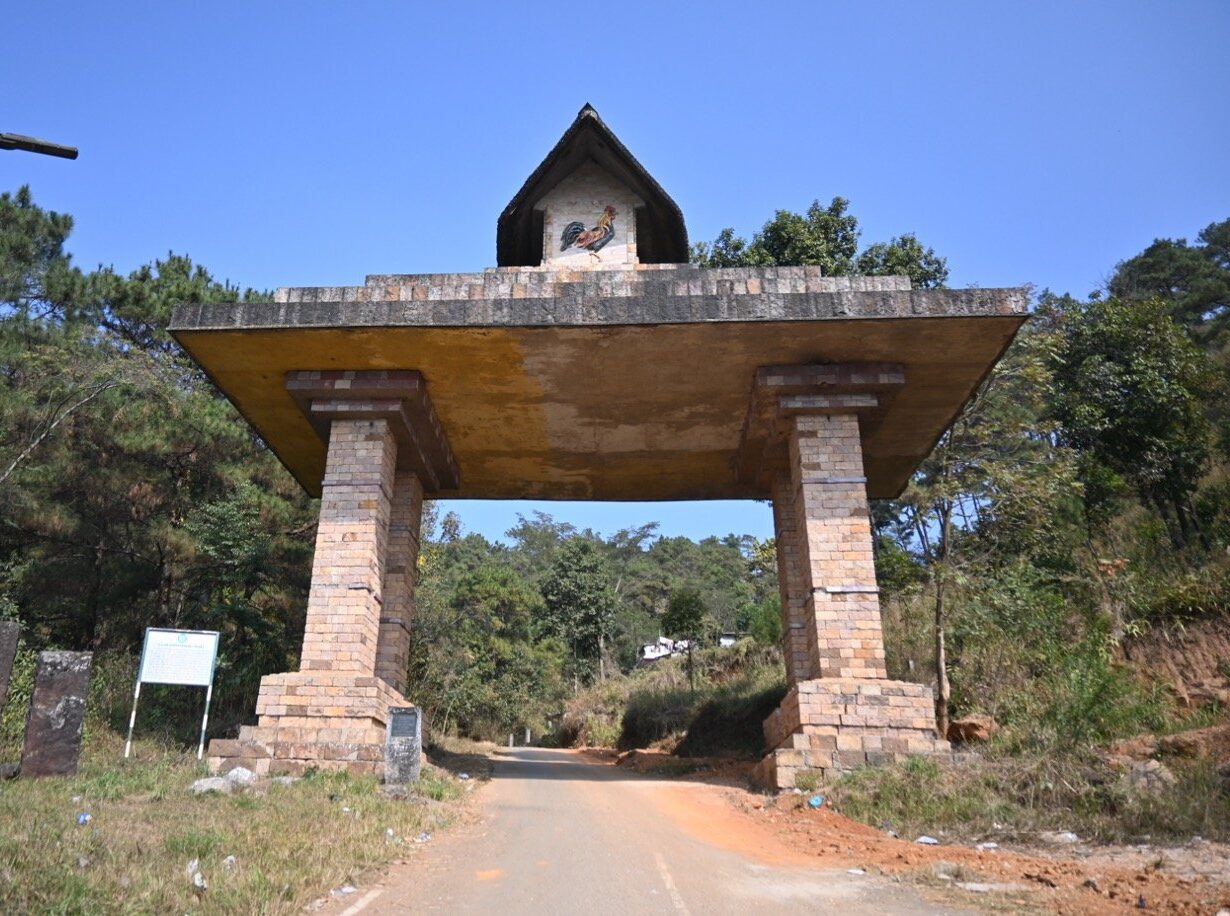 Stone gateway topped with a rooster emblem on the road to Lum Sohpetbneng, Meghalaya